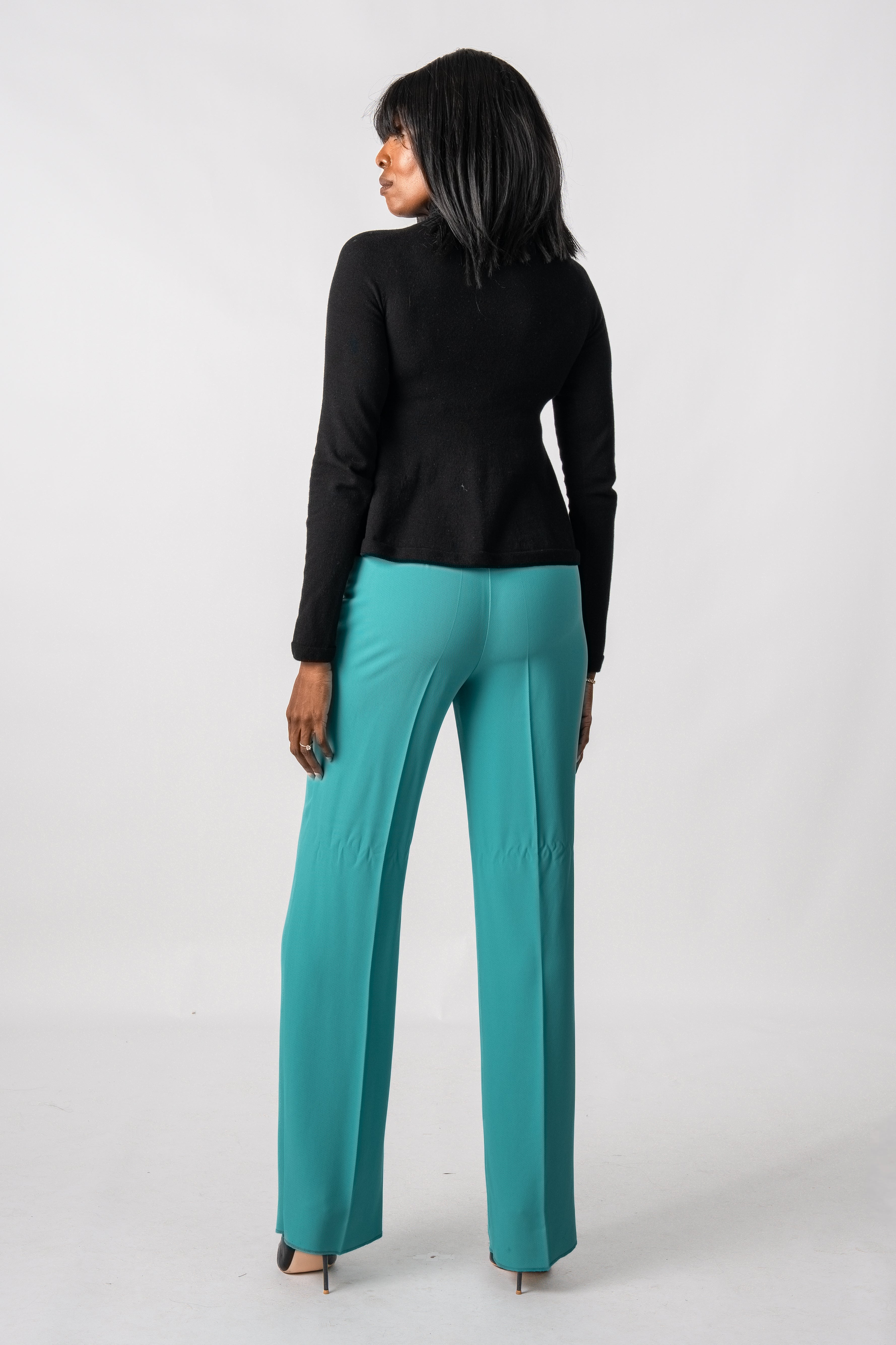 Woman wearing a black top and teal pants on a white background