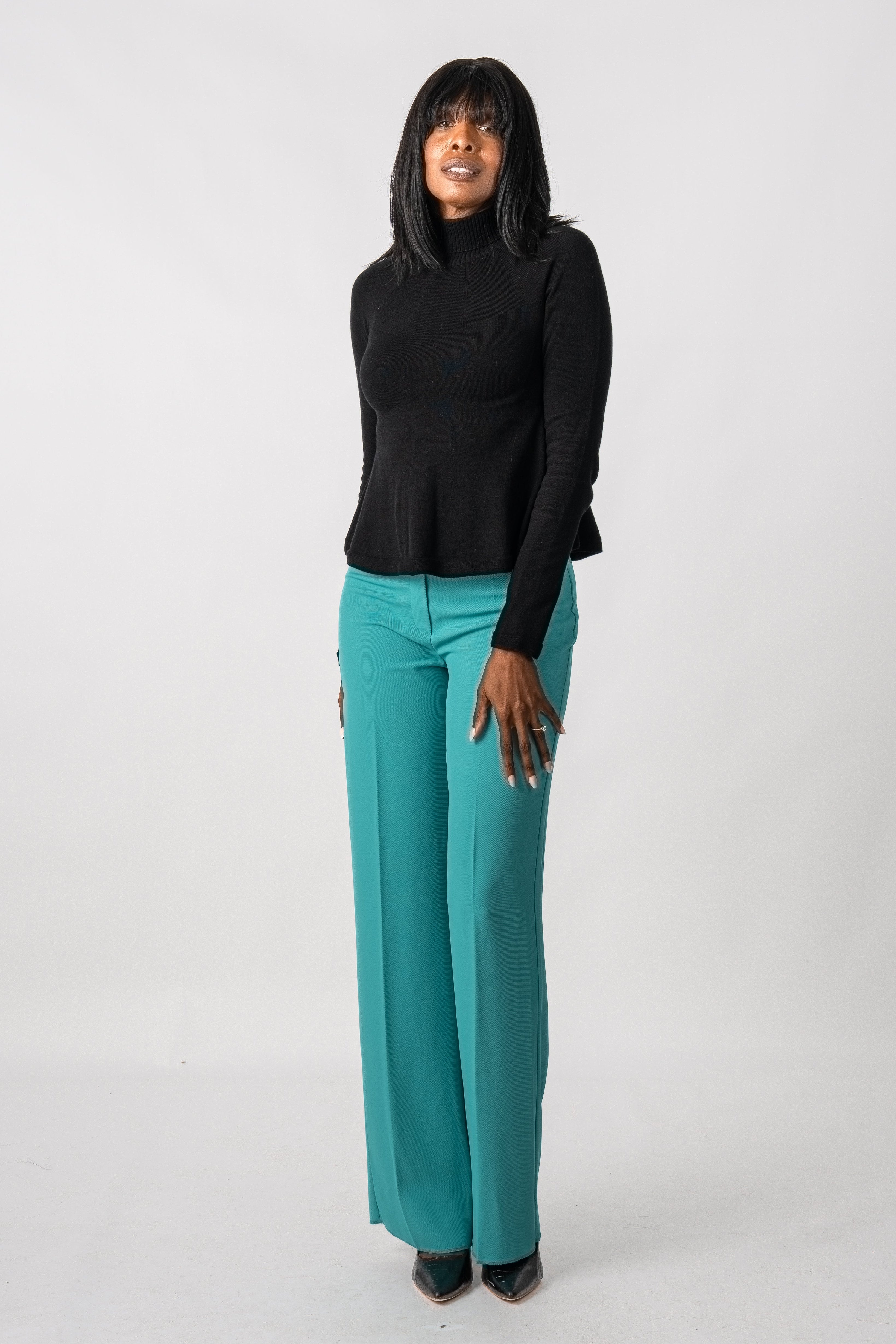 Woman wearing a black top and teal pants on a white background