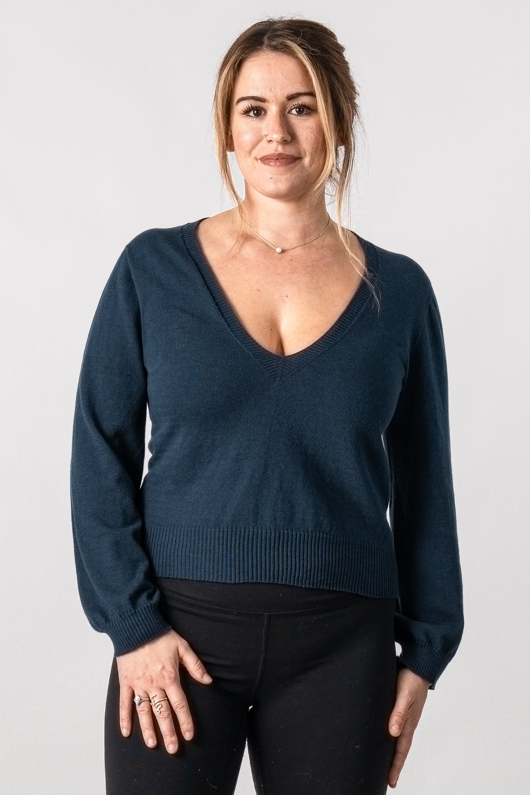 Woman wearing a dark blue sweater and black pants with knee-high boots on a white background