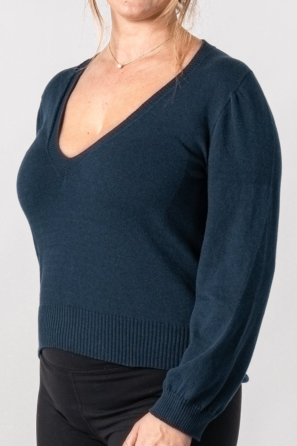 Woman wearing a dark blue long-sleeve top and black pants on a white background