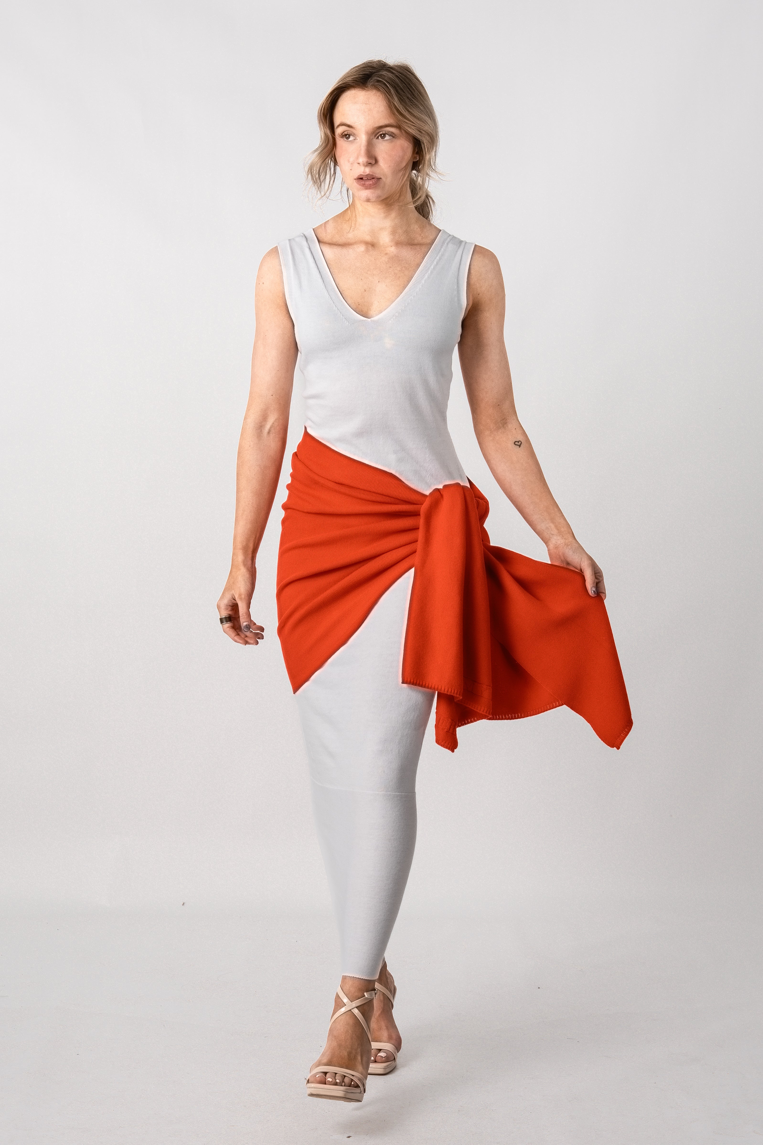 Woman wearing a white sleeveless top and white leggings with an orange skirt on a light gray background