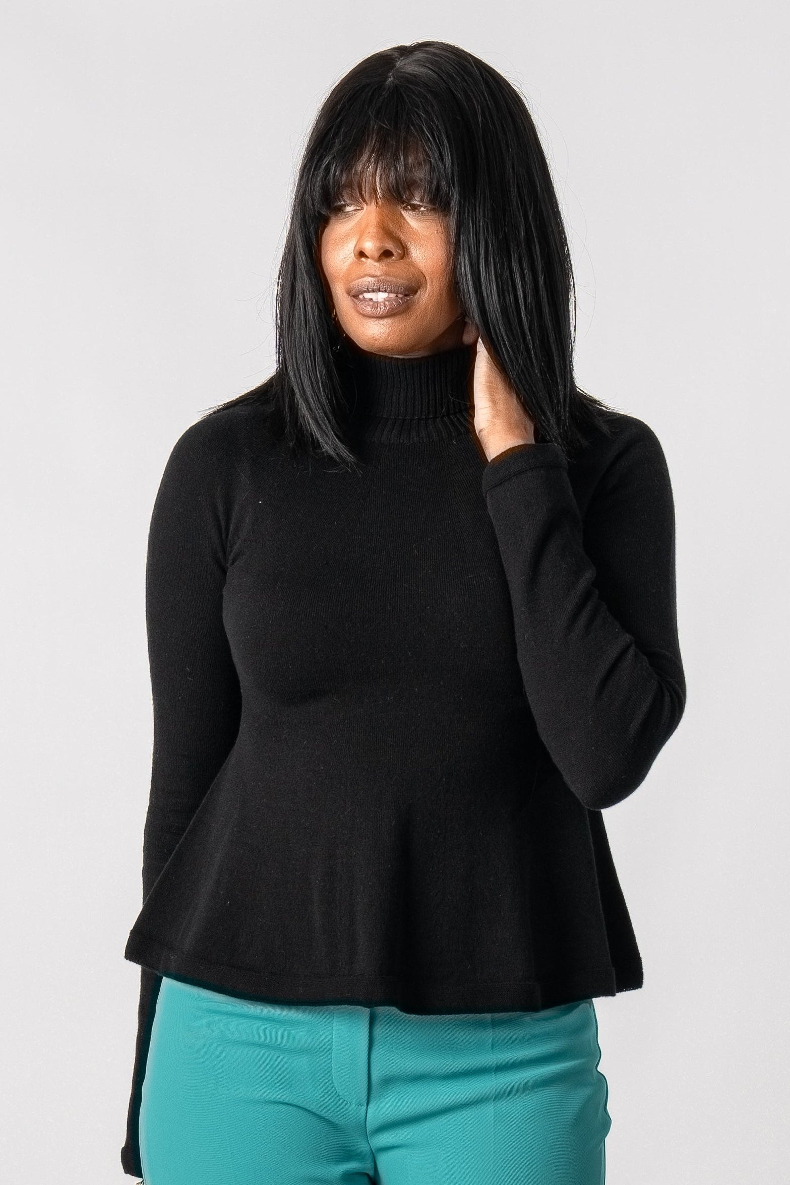 Woman wearing a black top and teal pants on a white background