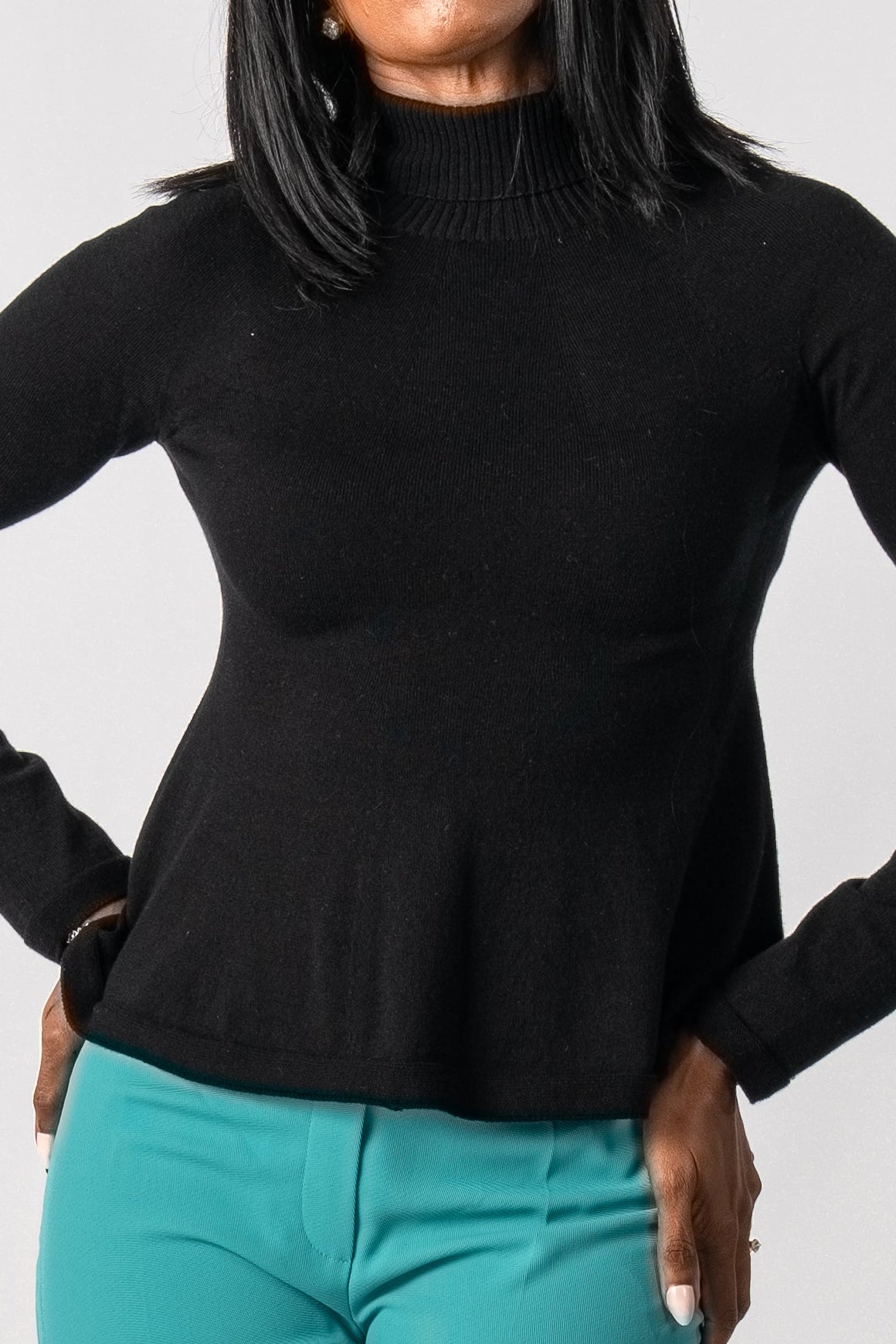 Person wearing a black turtleneck and teal pants on a white background