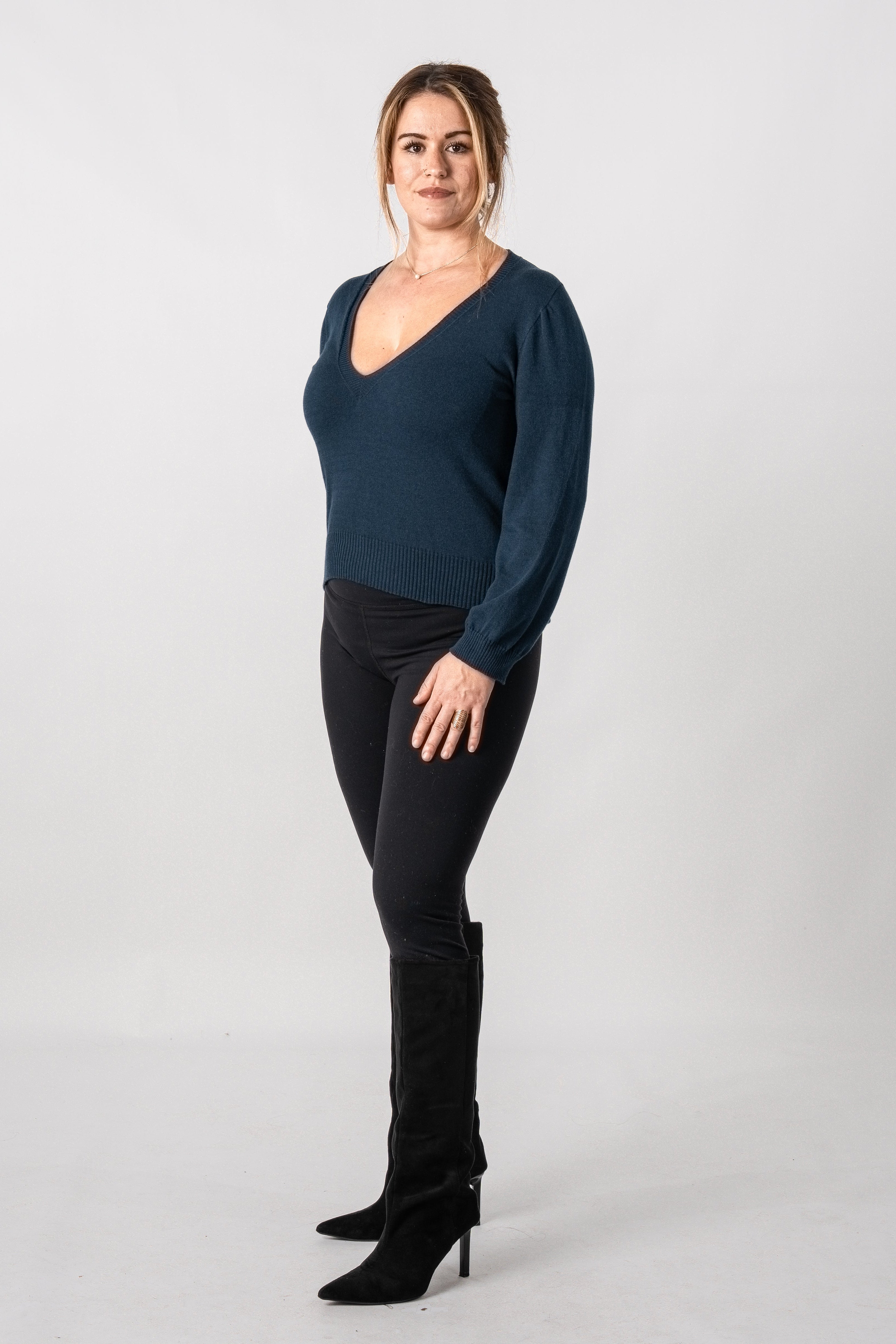 Woman wearing a dark blue long-sleeve top and black pants on a white background