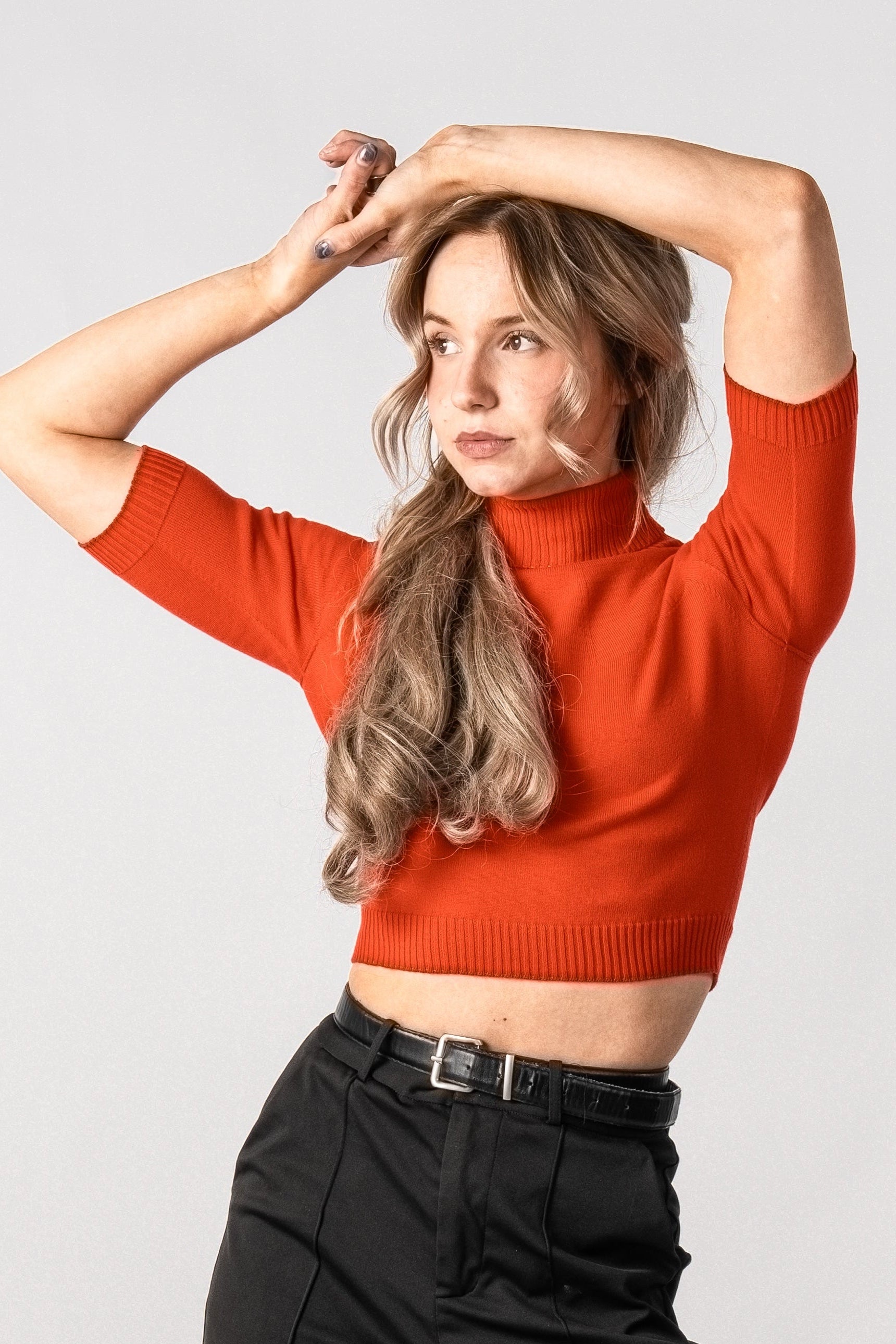 Woman wearing a red cropped top and black high-waisted pants on a light gray background